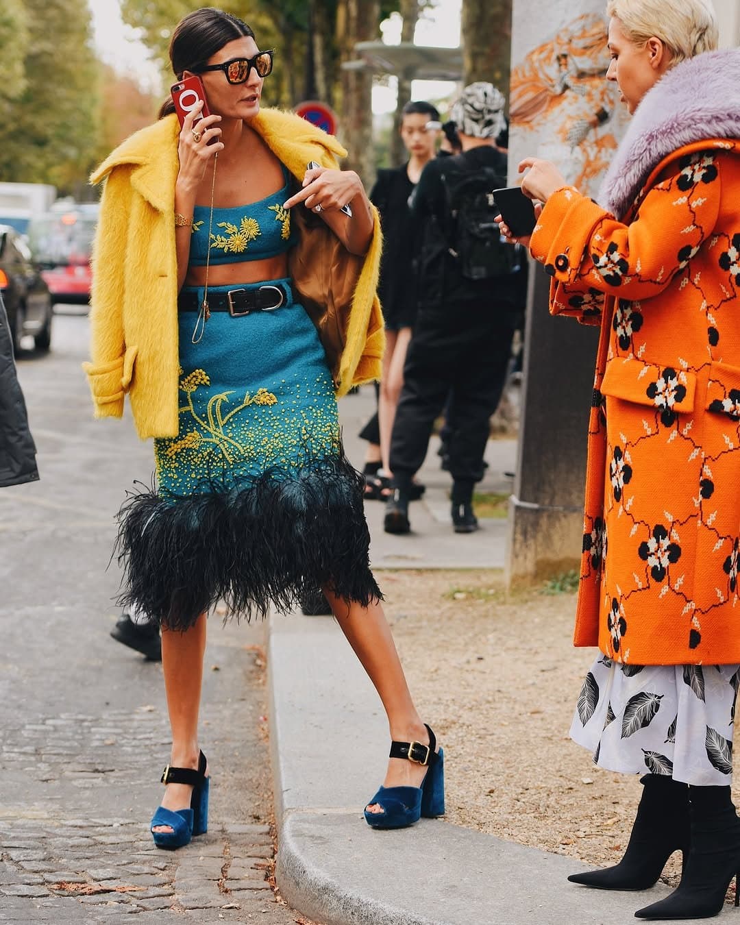 A teal embellished crop top and feather-trim skirt are styled with a bright yellow fuzzy coat, black belt, and blue platform heels.