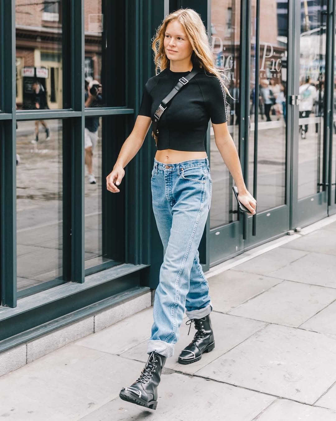 A fitted black cropped short-sleeve top is styled with light-wash cuffed jeans, black combat boots, and a black crossbody bag.
