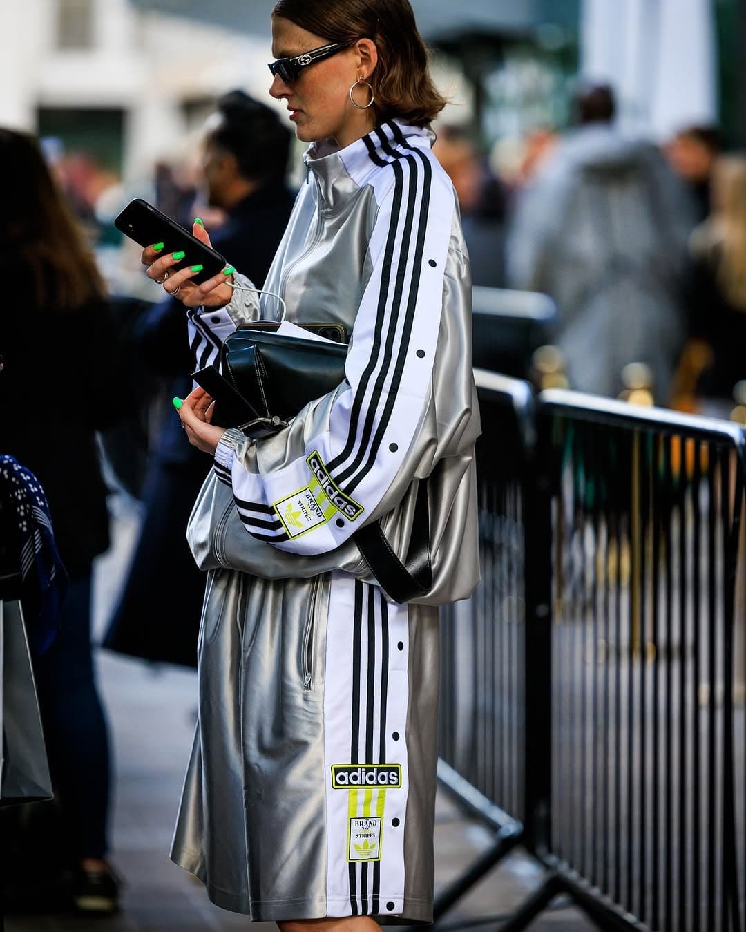 A metallic silver Adidas striped tracksuit-style look is styled with black sunglasses, hoop earrings, and a black shoulder bag.