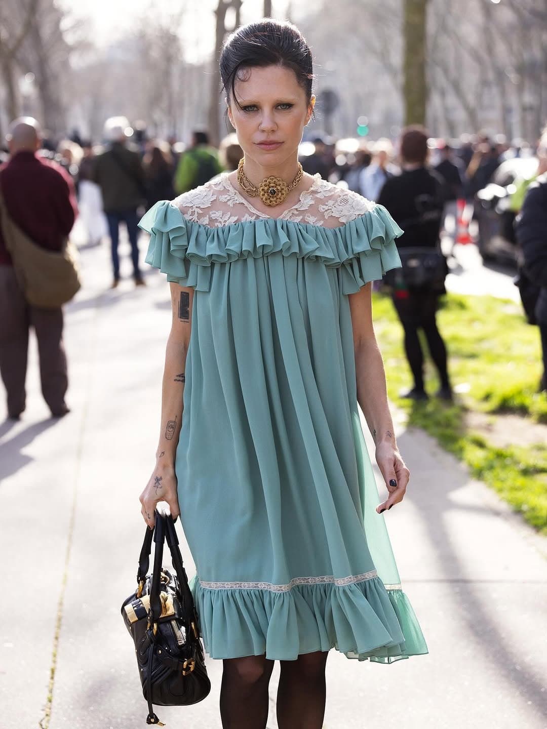 A mint ruffled lace-yoke dress is styled with black tights, a black handbag, and an ornate gold choker.