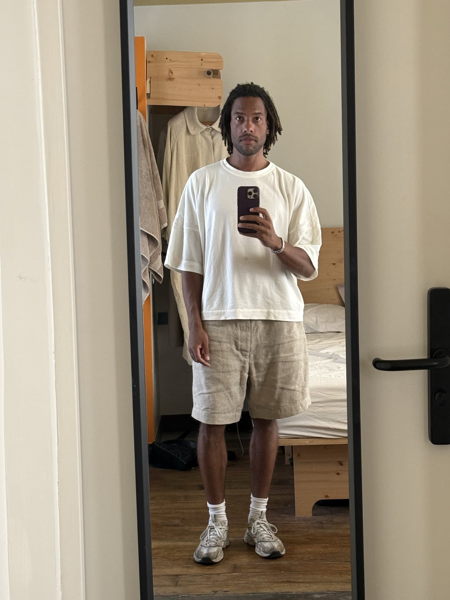 Oversized white T-shirt with beige linen shorts, white socks, and worn grey sneakers.