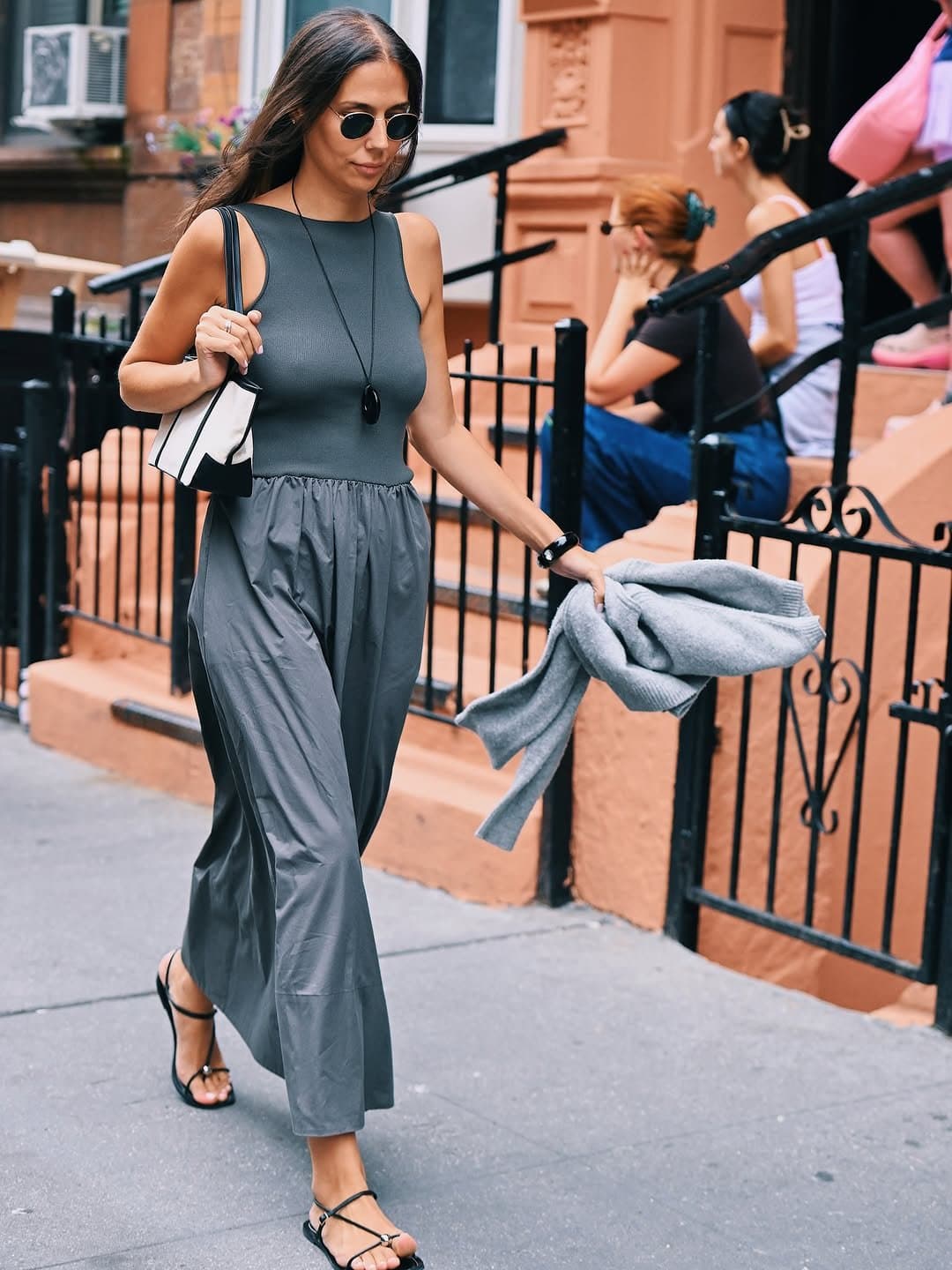 A tonal grey sleeveless dress is styled with black strappy flat sandals, round sunglasses, a pendant necklace, and a structured shoulder bag.